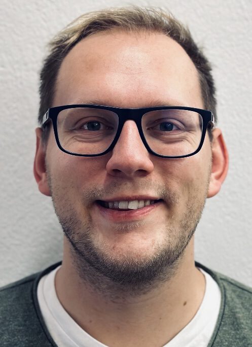 Erwachsener Mann mit kurzen Haaren und Brille lächelt in die Kamera