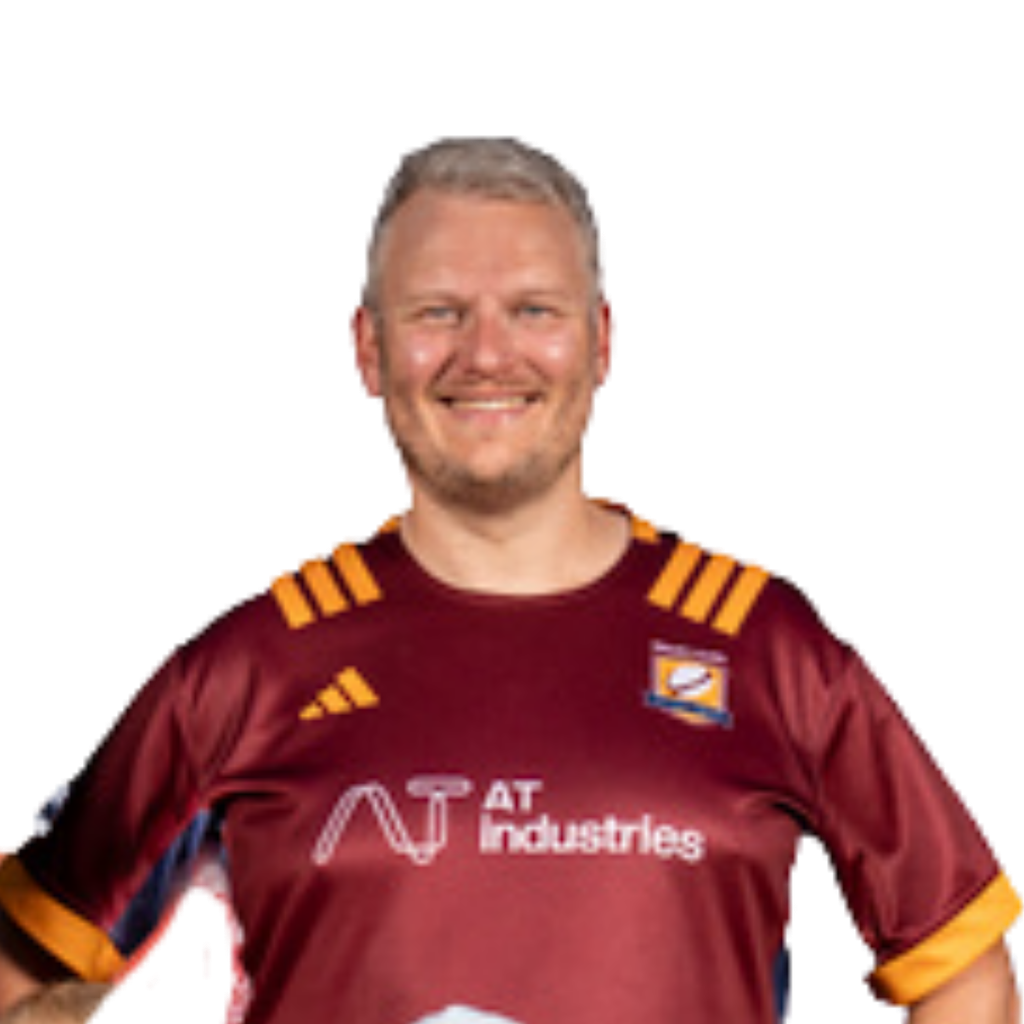Ein Mann mit blonden kurzen Haaren lächelt in die Kamera. Die Hände sind selbstbewusst in die Hüften gestemmt. Er trägt ein Rugby-Trikot